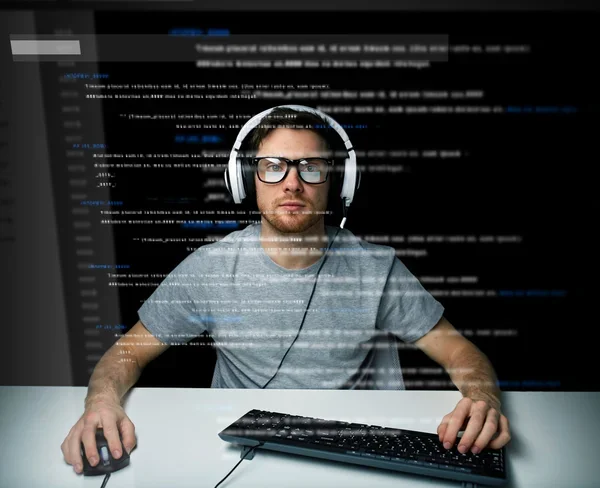 Developer in headphones and glasses at a keyboard behind a dark screen filled with code